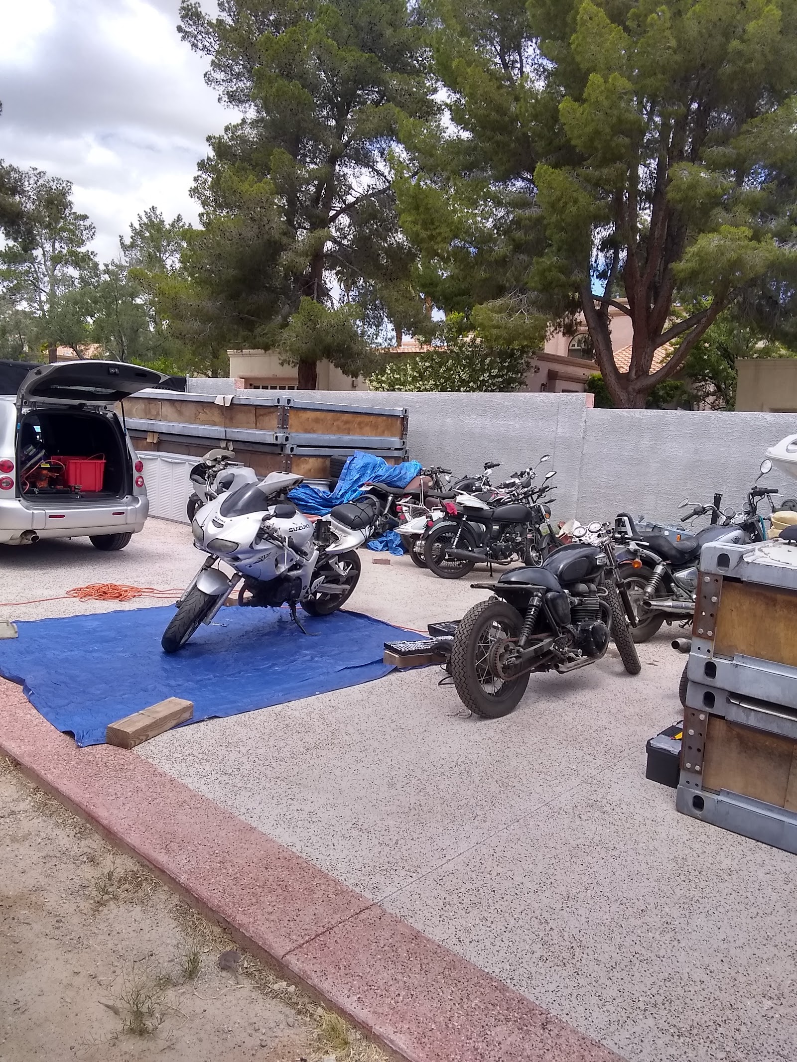 Multiple motorcycles and a van parked in a driveway work area